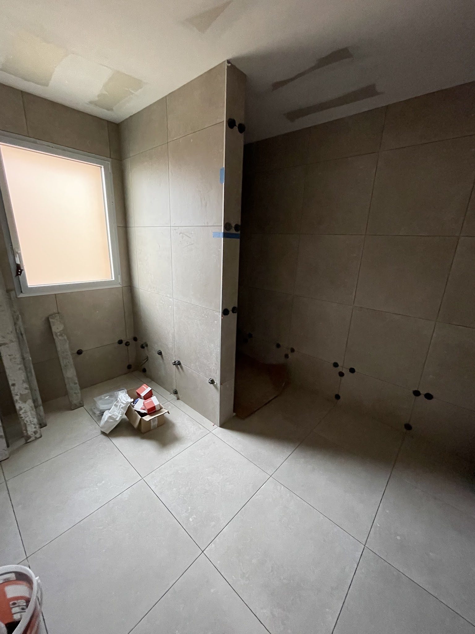Salle de bains en cours : grands carreaux aux murs et au sol, cales visibles
